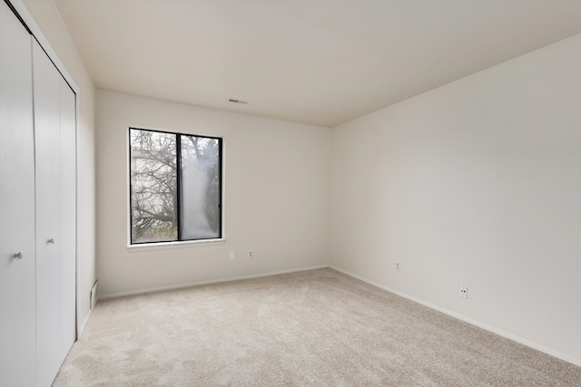 unfurnished bedroom with a closet, light colored carpet, visible vents, and baseboards