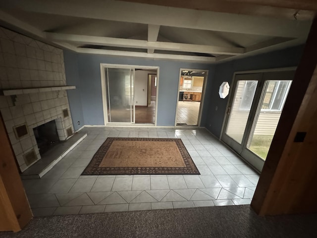 unfurnished living room featuring beamed ceiling, a fireplace, tile patterned flooring, and baseboards