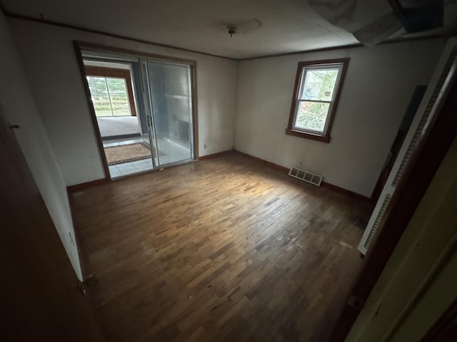 empty room featuring a wealth of natural light, wood finished floors, visible vents, and baseboards