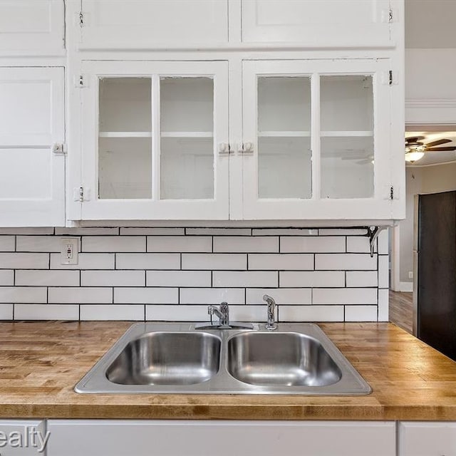 kitchen featuring tasteful backsplash, white cabinets, a sink, and glass insert cabinets