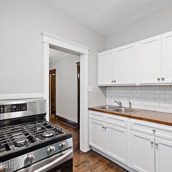 kitchen featuring decorative backsplash, dark wood-type flooring, white cabinets, stainless steel gas stove, and a sink