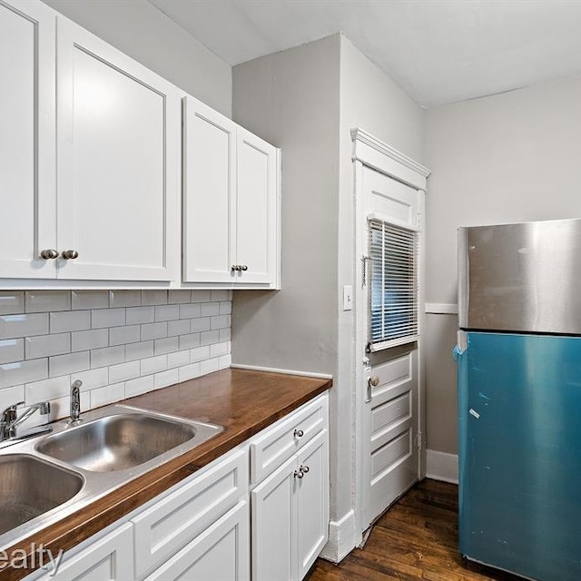 kitchen featuring decorative backsplash, dark wood-type flooring, freestanding refrigerator, white cabinetry, and a sink