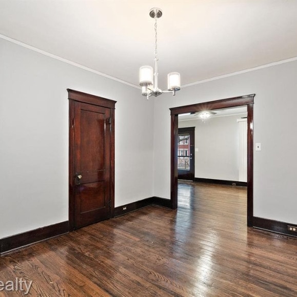 unfurnished room featuring ornamental molding, a notable chandelier, dark wood finished floors, and baseboards