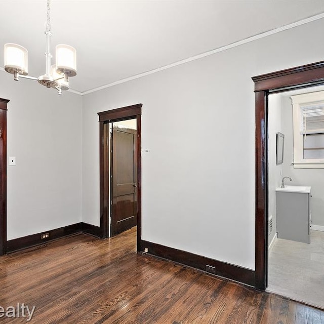 spare room with a sink, wood finished floors, baseboards, ornamental molding, and an inviting chandelier