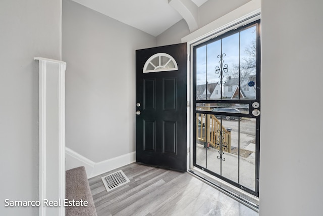 foyer featuring arched walkways, wood finished floors, visible vents, baseboards, and vaulted ceiling