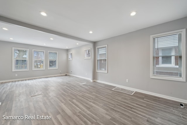 unfurnished living room with a healthy amount of sunlight, baseboards, visible vents, and wood finished floors