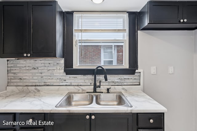 kitchen with light stone countertops, tasteful backsplash, dark cabinetry, and a sink