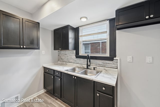 kitchen with baseboards, visible vents, a sink, light wood-type flooring, and backsplash