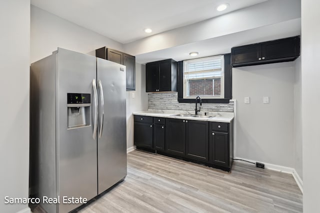 kitchen featuring stainless steel fridge, light wood-style flooring, a sink, light countertops, and backsplash