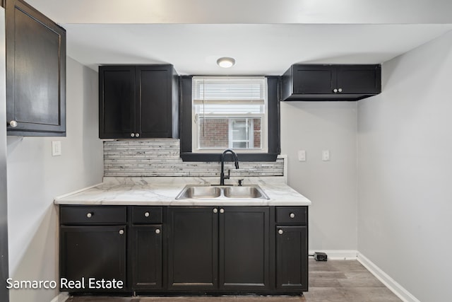 kitchen with wood finished floors, backsplash, a sink, and baseboards