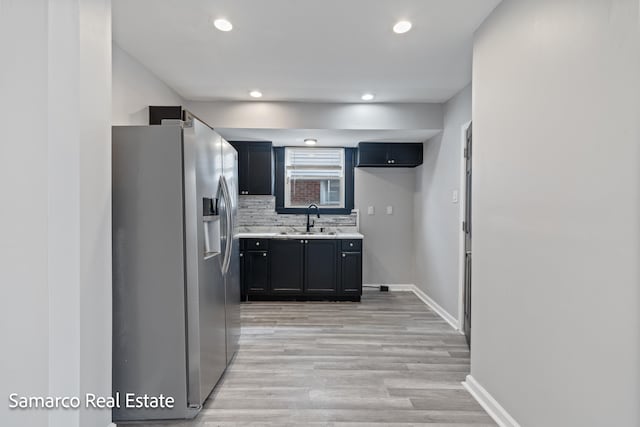 kitchen featuring dark cabinets, a sink, light countertops, stainless steel refrigerator with ice dispenser, and backsplash