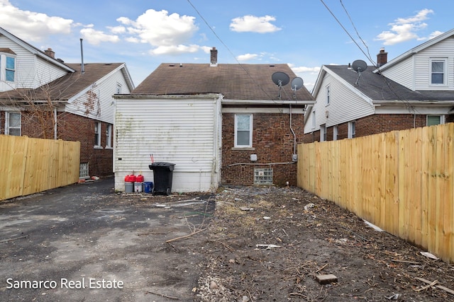 back of house featuring a chimney, fence, and brick siding