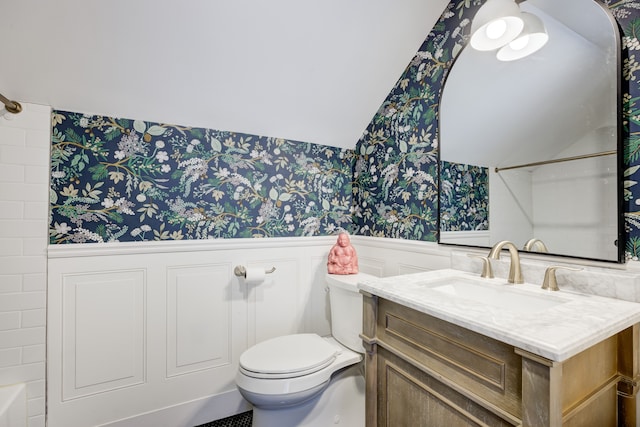 full bathroom with a wainscoted wall, vanity, toilet, and wallpapered walls