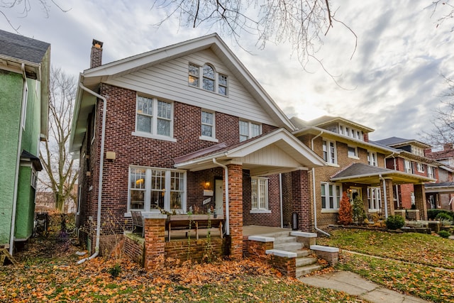 view of front of house featuring covered porch, brick siding, and a chimney