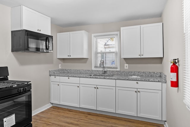 kitchen with baseboards, white cabinets, light stone countertops, black appliances, and a sink