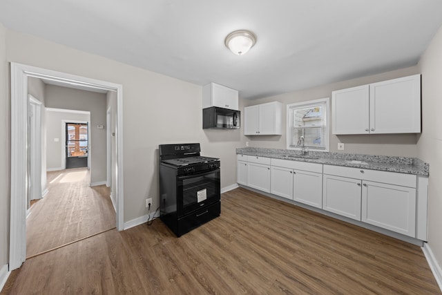 kitchen with baseboards, wood finished floors, black appliances, white cabinetry, and a sink