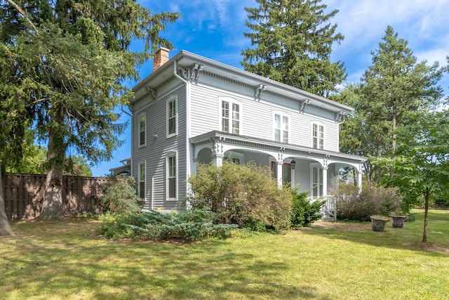 rear view of property featuring covered porch, a yard, a chimney, and fence