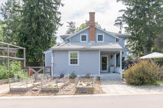 view of front facade with roof with shingles, a vegetable garden, a chimney, and fence