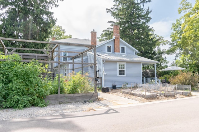 view of front of house with a shingled roof, a chimney, and a vegetable garden