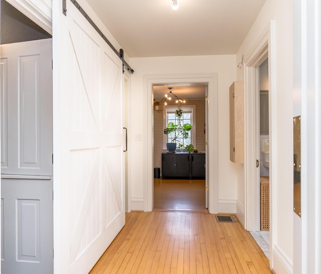 corridor featuring light wood finished floors, a barn door, visible vents, and baseboards