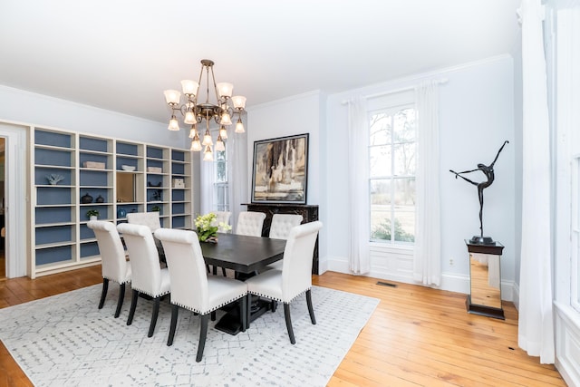 dining space featuring crown molding, a notable chandelier, light wood finished floors, visible vents, and baseboards