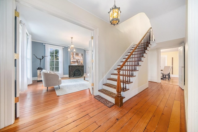 stairs featuring hardwood / wood-style flooring, baseboards, ornamental molding, and a chandelier