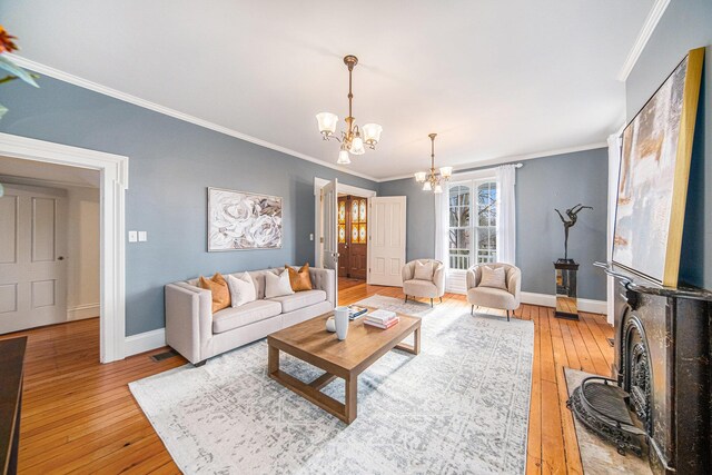 living area with crown molding, visible vents, light wood-style floors, a chandelier, and baseboards