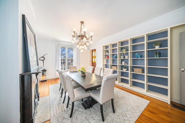 dining room with wood-type flooring, visible vents, ornamental molding, a chandelier, and baseboards