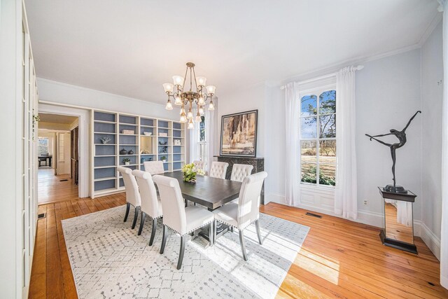 dining space with ornamental molding, visible vents, a notable chandelier, and light wood-style flooring