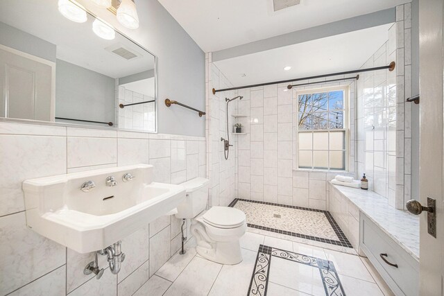 full bath featuring tile patterned flooring, toilet, visible vents, tile walls, and a tile shower