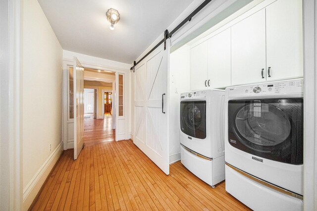 washroom with cabinet space, a barn door, light wood-style floors, washer and dryer, and baseboards