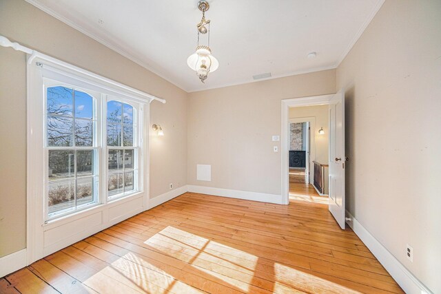 empty room with ornamental molding, light wood-type flooring, visible vents, and baseboards