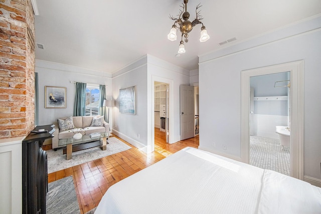 bedroom with visible vents, a spacious closet, ornamental molding, light wood finished floors, and an inviting chandelier