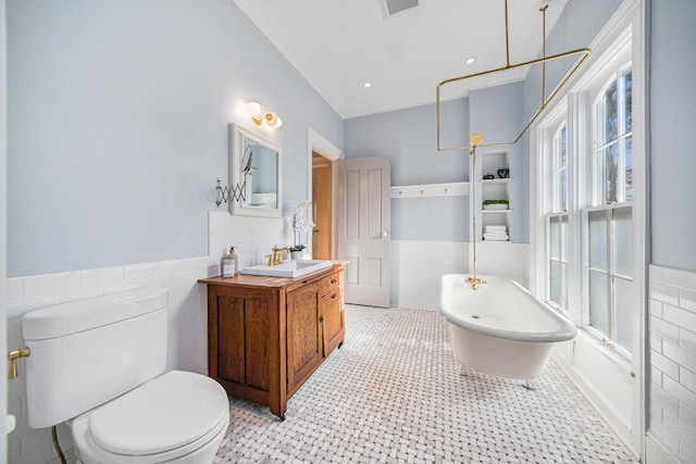 full bathroom with wainscoting, toilet, vanity, a freestanding tub, and tile walls