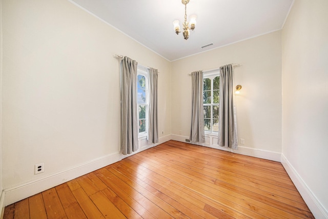 empty room featuring a chandelier, light wood-type flooring, and baseboards