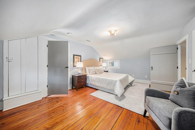 bedroom featuring lofted ceiling, light wood-style flooring, visible vents, and baseboards