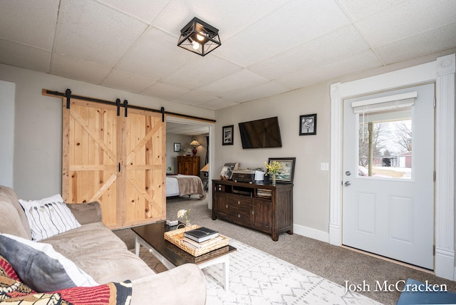 living room with a paneled ceiling, carpet, a barn door, and baseboards