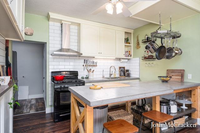 kitchen with decorative backsplash, dark wood-style flooring, black gas stove, wall chimney range hood, and a sink