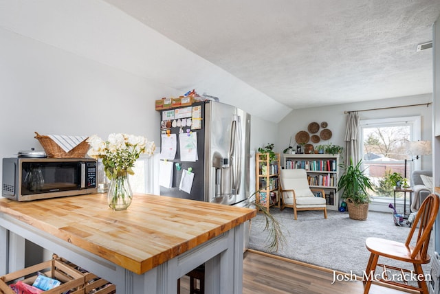 dining space featuring carpet flooring, vaulted ceiling, a textured ceiling, and wood finished floors