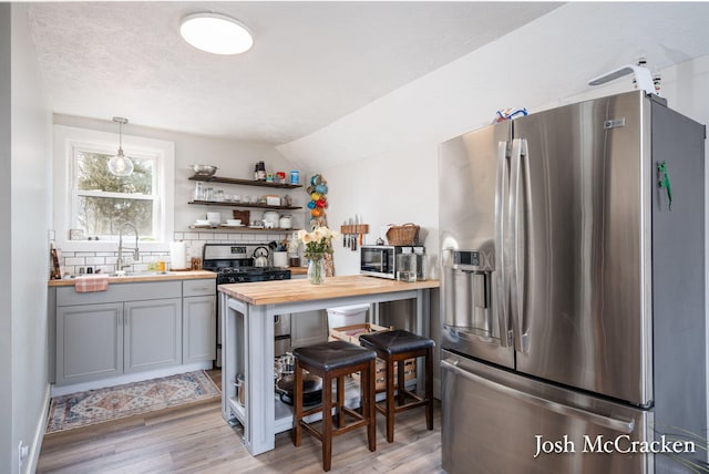 kitchen with butcher block counters, a sink, appliances with stainless steel finishes, light wood-type flooring, and backsplash