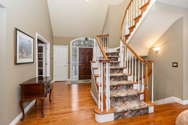 foyer entrance with stairs, high vaulted ceiling, wood finished floors, and baseboards