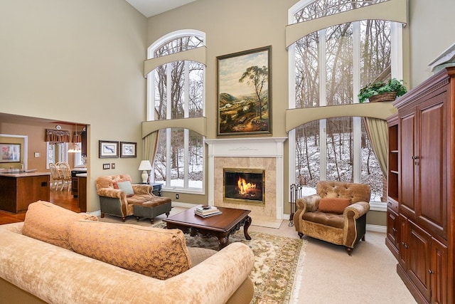 living area with a fireplace, light colored carpet, a towering ceiling, and a healthy amount of sunlight