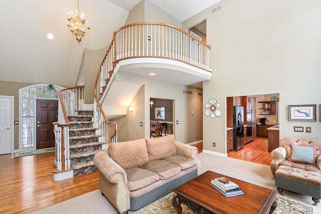 living room with a notable chandelier, visible vents, light wood-style floors, baseboards, and stairs