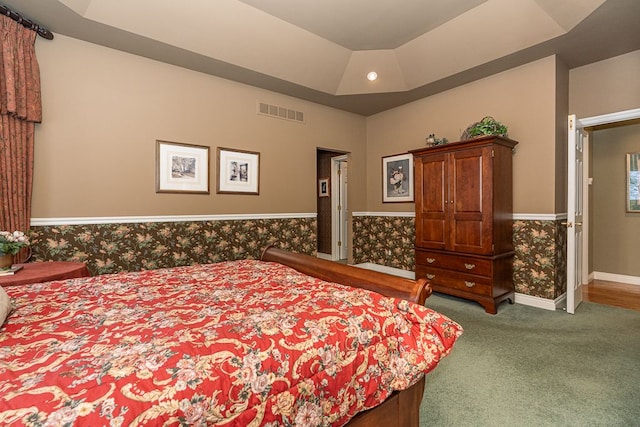 carpeted bedroom featuring a tray ceiling, a wainscoted wall, visible vents, baseboards, and wallpapered walls