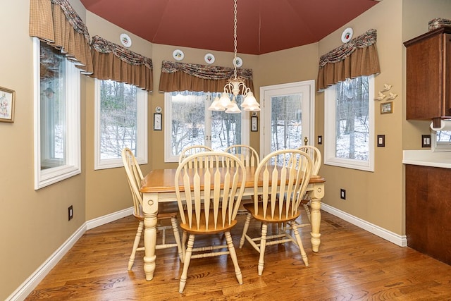 dining area with an inviting chandelier, vaulted ceiling, baseboards, and wood finished floors