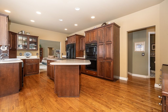 kitchen featuring wood finished floors, a center island, light countertops, black appliances, and a sink