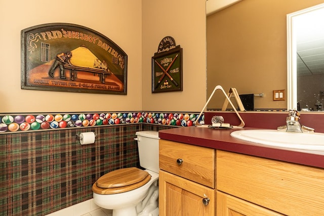 half bathroom with tile patterned flooring, wainscoting, vanity, and toilet