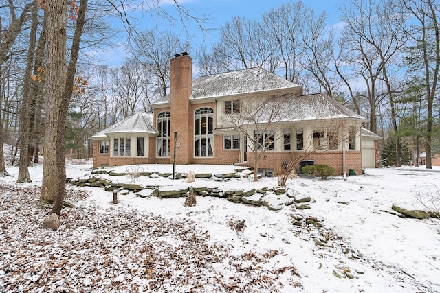 snow covered rear of property with a chimney and brick siding