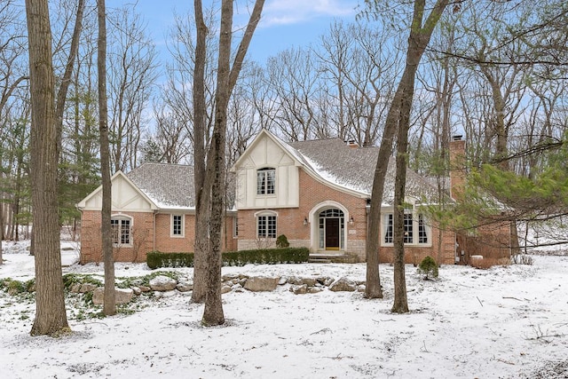 english style home featuring roof with shingles, brick siding, and a chimney