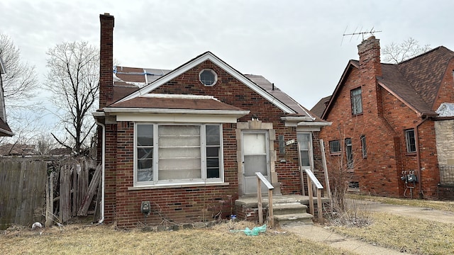 view of front of house with brick siding, fence, and a chimney